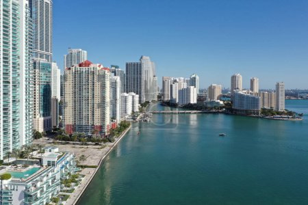 Aerial image of waterfront residential buildings in Brickell neighborhood of Miami, Florida reflected in calm water of Biscayne Bay on sunny morning.