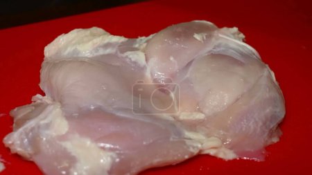 Photo for A gloved hand skillfully uses a knife on a red cutting board to trim a chicken fillet, removing the skin, hymen, and excess fat for a clean, ready-to-cook piece - Royalty Free Image