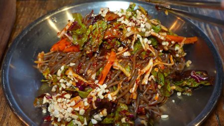 A plate of fresh soba noodles, garnished with herbs, vegetables, sesame seeds, and a glossy sauce.