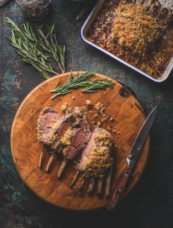 Photo for Tasty medium rare roasted lamb ribs with crust on wooden cutting board with rosemary and knife. Top view. Meat food, racks of lamb - Royalty Free Image