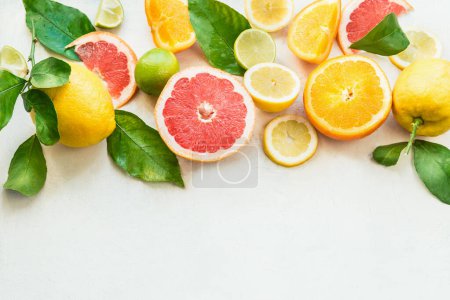Various citrus fruits border with green leaves on white background. Top view. Halves of citrus. Vitamin C. Healthy natural immune boosters