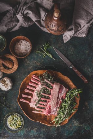 Photo for Lamb racks cooking preparation. Raw lamb ribs with fresh rosemary and time on wooden cutting board on dark rustic kitchen table background. Top view. Meat food - Royalty Free Image