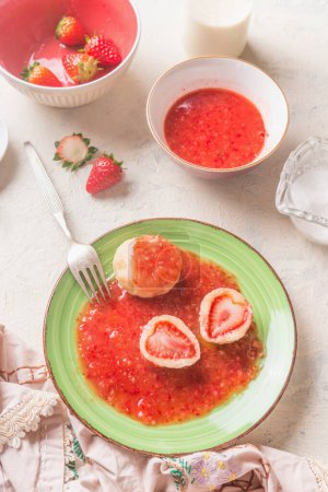 Foto de Close up of tasty boiled cottage dumplings stuffed  with fresh strawberries with sweet berries sauce on white kitchen table. Top view. Summer sweet food. Home cooking. Seasonal meal. Knedliki . - Imagen libre de derechos
