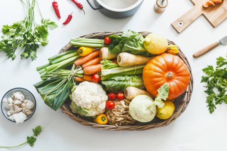 Various harvest organic vegetables for tasty cooking and eating in wooden tray on white desktop with kitchen utensils herbs and spices, top view. Healthy lifestyle. Local vegetarian food. Zero waste