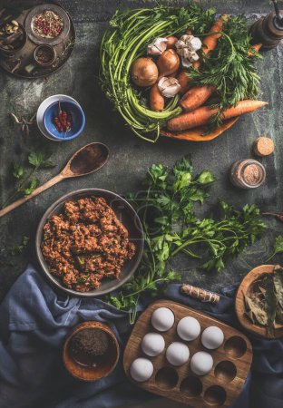 Tasty cooking. Flavored minced meat in wooden bowl with vegetables , herbs and spices ingredients, cooking spoon on dark rustic background. Top view. Home still life. Stuffing cooking preparation