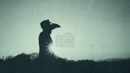 A mysterious horror figure wearing a plague doctor crow mask. Silhouetted against the sun on a winters day. With a grunge, grainy vintage edit.