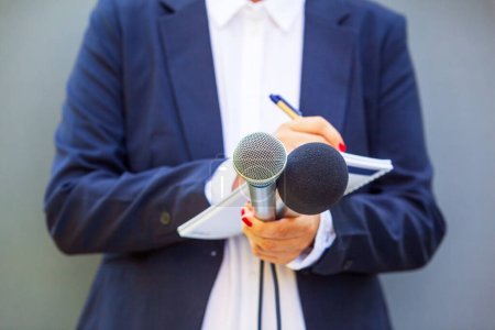 Periodista en conferencia de prensa o evento mediático, escribiendo notas, sosteniendo micrófono