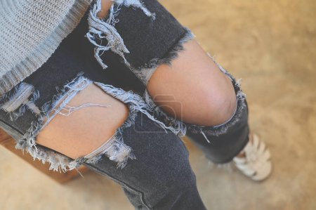 Photo for Torn pants , torn jeans, close up girl wear jean - women knees in jeans holes in jeans, fashion clothing. Hips and knees in fashionable jeans - Royalty Free Image