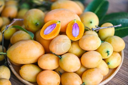 Foto de Ciruela mariana y hojas en plato sobre fondo de madera, fruta tropical Nombre en Tailandia Ciruela mariana amarilla dulce Maprang Plango o Mayong chid - Imagen libre de derechos