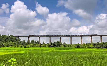 Photo for Super fast train crosses long viaduct at scenic location of green fields on Konkan Railway route. - Royalty Free Image