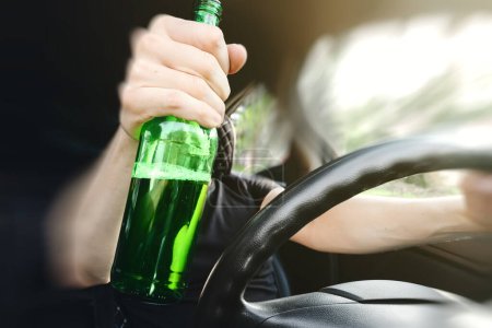Foto de Primer plano de una botella de alcohol en la mano del conductor al volante del coche. Concepto de conducción de alcohol. - Imagen libre de derechos
