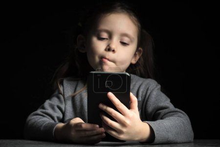 Kid girl with a thoughtful face at night communicates on Internet. Child gadget addiction and insomnia, psychological problems.