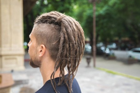 Téléchargez les photos : Back view of a caucasian man with dreadlocks and sidecut on a summer street. - en image libre de droit