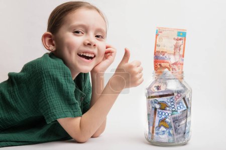 Photo for Kid with a large transparent jar with Kazakhstani tenge money. Bank account for a child. - Royalty Free Image
