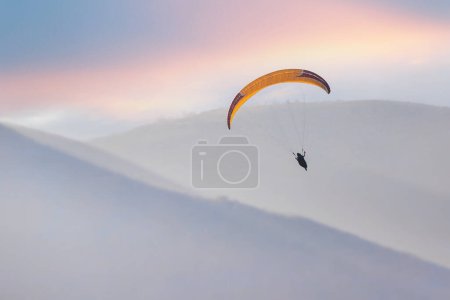 Téléchargez les photos : Un parapente planifie dans le ciel dans une région vallonnée. - en image libre de droit