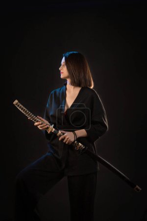 Foto de Joven hermosa mujer en kimono negro con espada japonesa sobre fondo negro. - Imagen libre de derechos