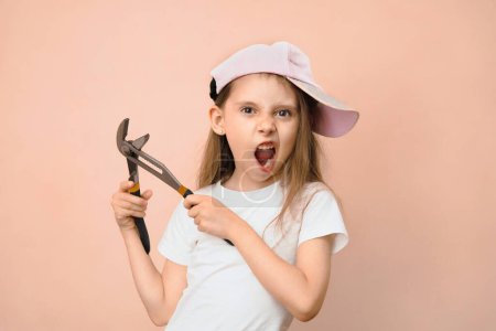 Photo for Caucasian girl of primary school age in a baseball cap with a wrench on a pink background, fathers daughter tomboy. - Royalty Free Image
