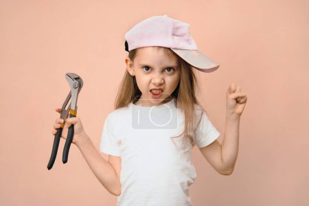 Photo for Cute little girl of primary school age in a baseball cap with a wrench on a pink background, dads upbringing. - Royalty Free Image