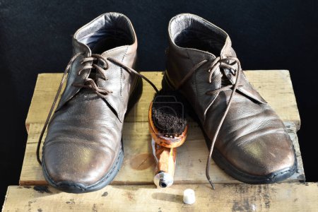 Photo for A pair of leather boots are on a chair, and a shoe brush with cream for cleaning them lies nearby. - Royalty Free Image
