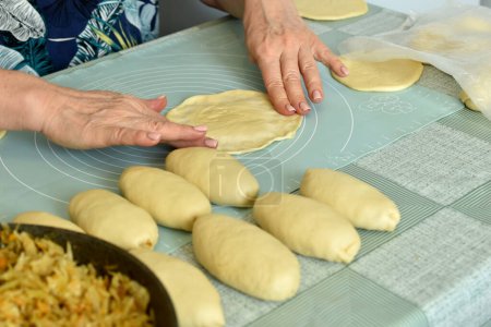 Photo for The baker at the table prepares the dough to be filled with ago filling. - Royalty Free Image