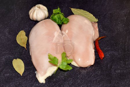 Carne de pollo cruda, pechuga, lista para cocinar se encuentra sobre un fondo oscuro, vista superior.