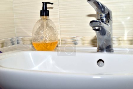 On the washbasin in the bathroom there is a bottle of yellow liquid soap.
