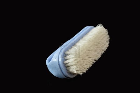 A clothes brush with plastic bristles lies on a black background.