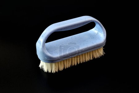 A clothes brush with plastic bristles lies on a black background, top view.