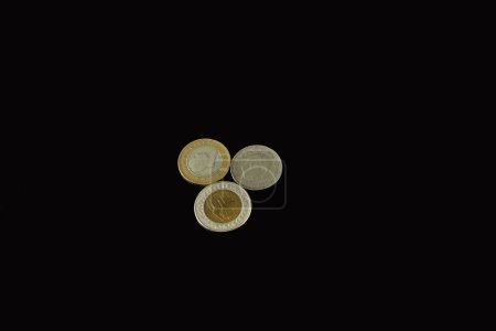 Several metal coins of different denominations lie on a black background.