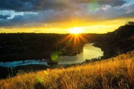 Téléchargez les photos : Bright cloudy sunset time landscape with grass and river highlighted by sunlight. Ukrainian rural scenery - en image libre de droit