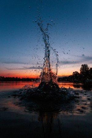 Téléchargez les photos : Splash on a lake water at the sunset time. At the summertime. Reflection on a water surface - en image libre de droit