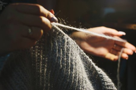 Téléchargez les photos : Close up hands knitting the dress from light blue wool on blurry background. Using circular needles - en image libre de droit