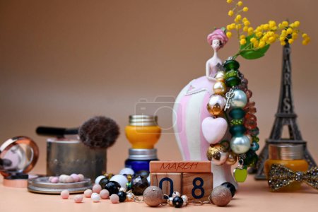A wooden calendar with the date March 8 stands surrounded by a variety of women's accessories against the background of a porcelain figurine of a flower girl.