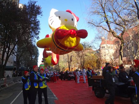 Foto de NUEVA YORK CITY, 23 DE NOVIEMBRE DE 2017: Macy 's Thanksgiving Day Parade. Visto poco antes de unirse al desfile está el globo gigante del personaje "Hello Kitty" volando su avión. También se muestran numerosos manipuladores de globos y otro personal de desfile. - Imagen libre de derechos