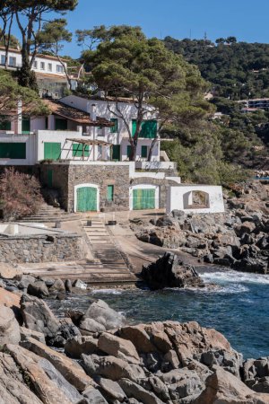 Fisherman's beautiful hut with green doors in a rocky cliff landscape quiet water's edge in Mediterranean Sea, Costa Brava