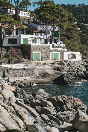 Fisherman's beautiful hut with green doors in a rocky cliff landscape quiet water's edge in Mediterranean Sea, Costa Brava