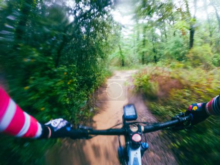 Schnelles Fahren mit dem Mountainbike auf einer einspurigen Straße, Fahrersicht in einer schlammigen Waldlandschaft