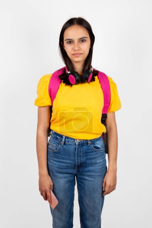 Foto de Retrato de una adolescente algo torpe y seria con mochila y auriculares sosteniendo un teléfono móvil - Imagen libre de derechos