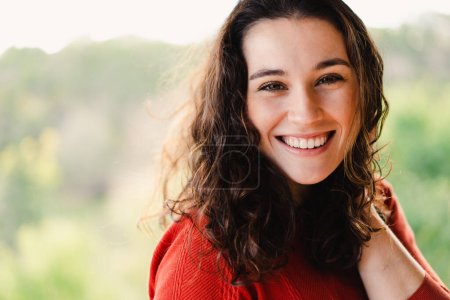 Photo for Young happy beautiful brunette woman smiling to camera and holding hair in a windy day outdoors. Natural beauty with a healthy smile - Royalty Free Image