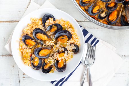 Téléchargez les photos : Bouillon de riz aux moules cuit avec des légumes et du vin blanc servi dans un plat blanc. Vue du dessus - en image libre de droit