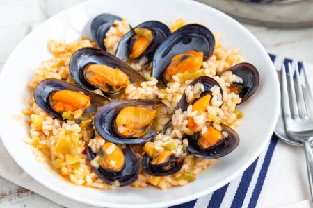 Téléchargez les photos : Bouillon de riz aux moules cuit avec des légumes et du vin blanc servi dans un plat blanc. - en image libre de droit