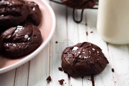 Téléchargez les photos : Délicieux en-cas de biscuits maison brownie avec dessus fissuré et saupoudré de flocons de sel sur la table et une petite bouteille de lait. Gros plan - en image libre de droit