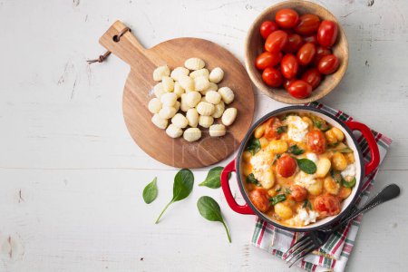 Téléchargez les photos : Casserole de gnocchi à la sauce tomate crémeuse aux épinards et mozzarella fondue sur table en bois peinte en blanc. Vue du dessus - en image libre de droit