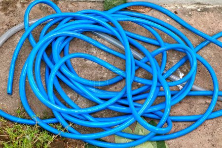Photo for Spiral blue hoses laying on the ground next to a green leaf. - Royalty Free Image