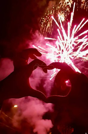 Foto de Una fotografía de una persona haciendo una forma de corazón con sus manos, alguien haciendo una forma de corazón con sus manos con fuegos artificiales en el fondo. - Imagen libre de derechos