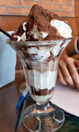 Foto de Una fotografía de un helado de postre con crema batida y chocolate, hay un postre en una taza de vidrio sobre una mesa. - Imagen libre de derechos