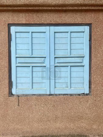 Téléchargez les photos : Une photographie d'une fenêtre bleue avec un chat assis sur le rebord, il y a une fenêtre bleue avec un volet bleu sur un bâtiment bronzé. - en image libre de droit