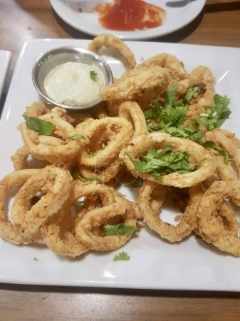Photo for A photography of a plate of fried onion rings with a side of dip, there is a plate of fried squid rings with a dipping sauce. - Royalty Free Image