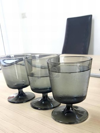 Foto de Una fotografía de tres vasos sentados en una mesa con un portátil en el fondo, tres vasos de agua sentados en una mesa con un portátil en el fondo. - Imagen libre de derechos