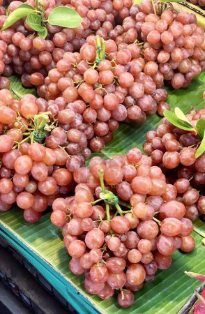 Photo for A photography of a bunch of grapes on a banana leaf, grocery store display of grapes on banana leaf tray with green leaves. - Royalty Free Image